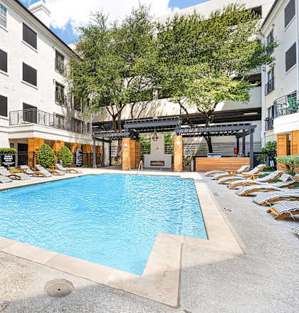 an outdoor pool with lounge chairs and trees in front of an apartment building