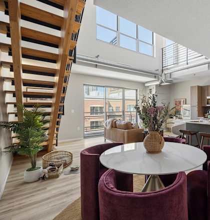 A modern kitchen with a dining table and chairs in the foreground and a staircase on the left.