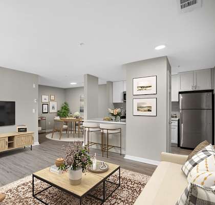 A modern living room with a flat screen TV, a coffee table, and a kitchen area in the background.