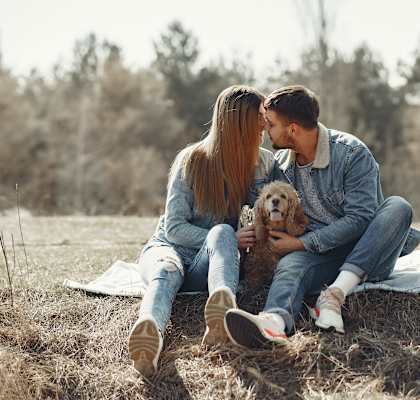 a couple kissing while sitting on a blanket with their dog in a field