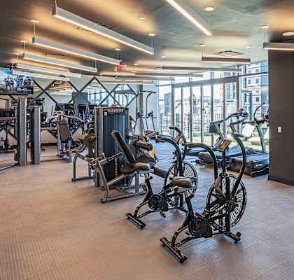 Interior of the well-equipped fitness center at 3THIRTY3 Apartments, featuring exercise machines, weights, and ample natural light.