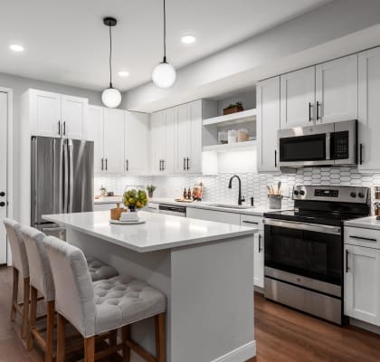 a kitchen with white cabinets and a large island with white chairs at The Flats & Terraces at Wildhorse Village, Chesterfield, MO