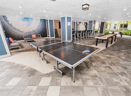 A ping pong table is in the middle of a room with a blue wall and a mural. at CODA Apartments , Orlando, FL, 32826