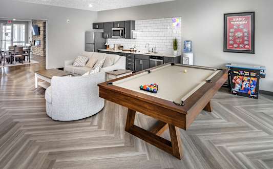 A pool table is in the middle of a room with a white couch and a wooden coffee table.