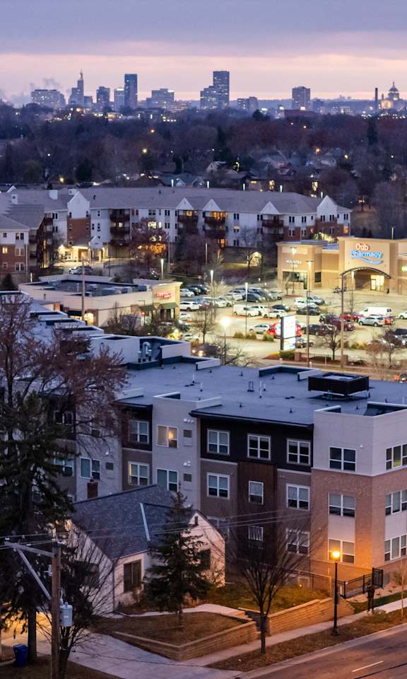 A cityscape at dusk with a lit up shopping center in the foreground.