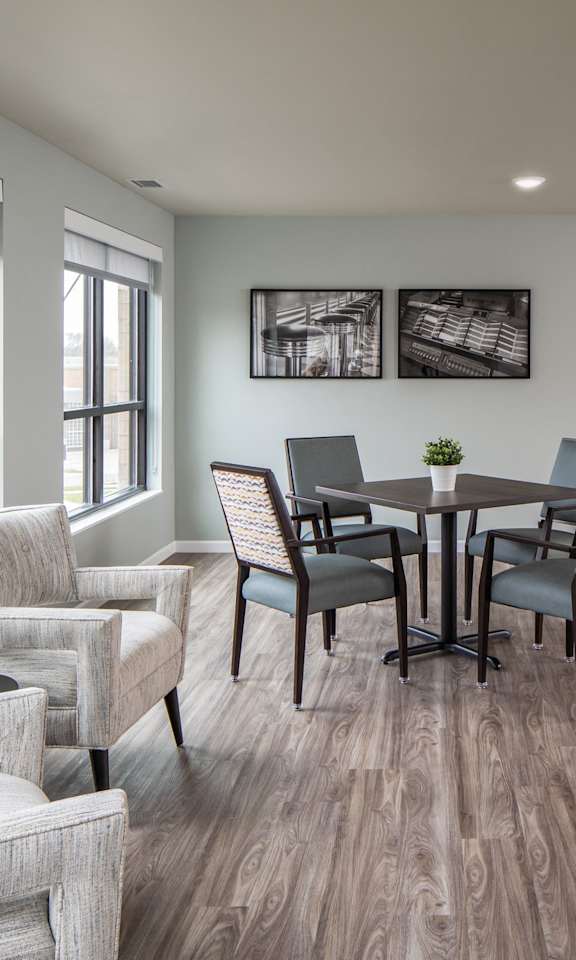 A living room with a grey sofa, a grey armchair, a grey chair, a grey coffee table, a black television, a small table with a plant on it, and a wall with a picture and a mirror.