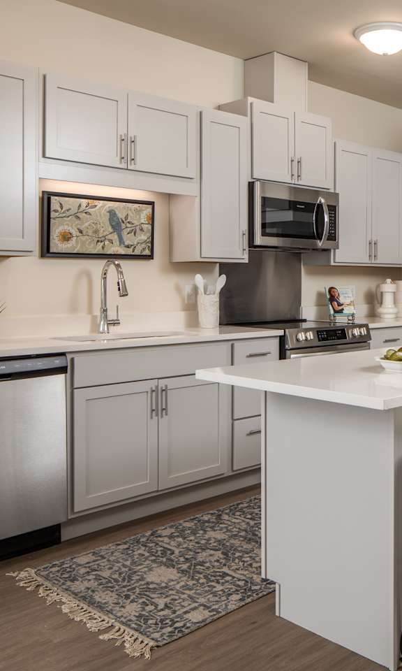 A kitchen with white cabinets and a white island with two chairs.