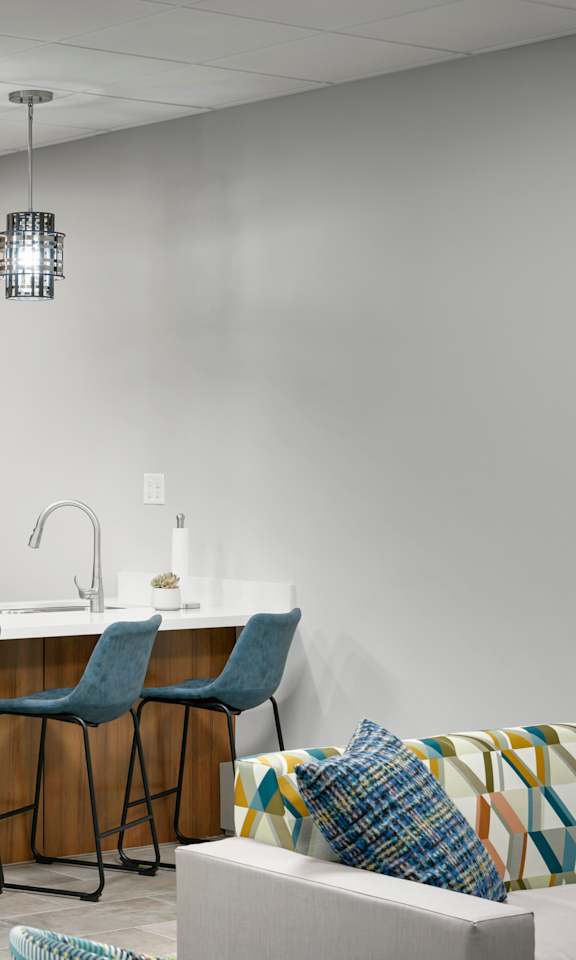 A kitchen with a refrigerator, bar stools, and a dining table.