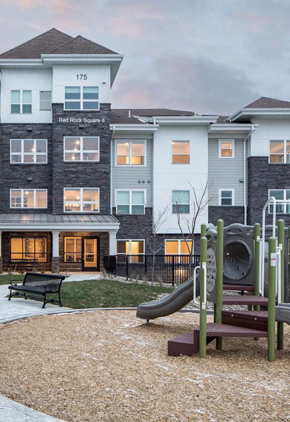 A playground with a slide and a bench in front of a multi-story residential building.