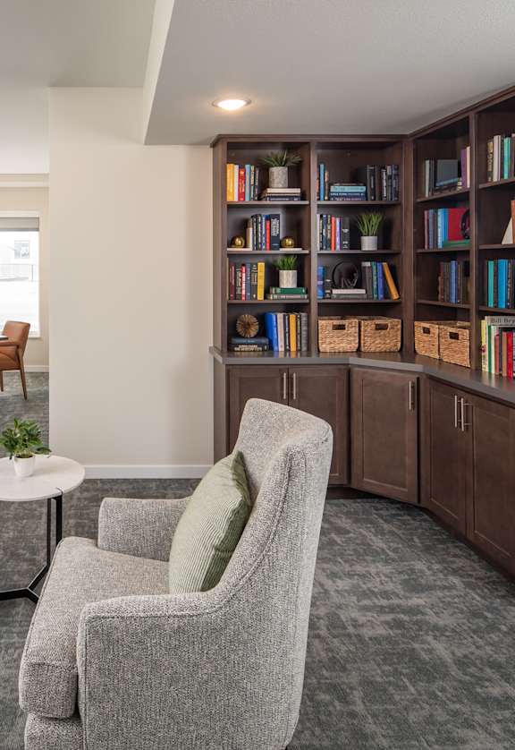 A living room with a grey sofa, a grey armchair, a coffee table, and a bookshelf filled with books.