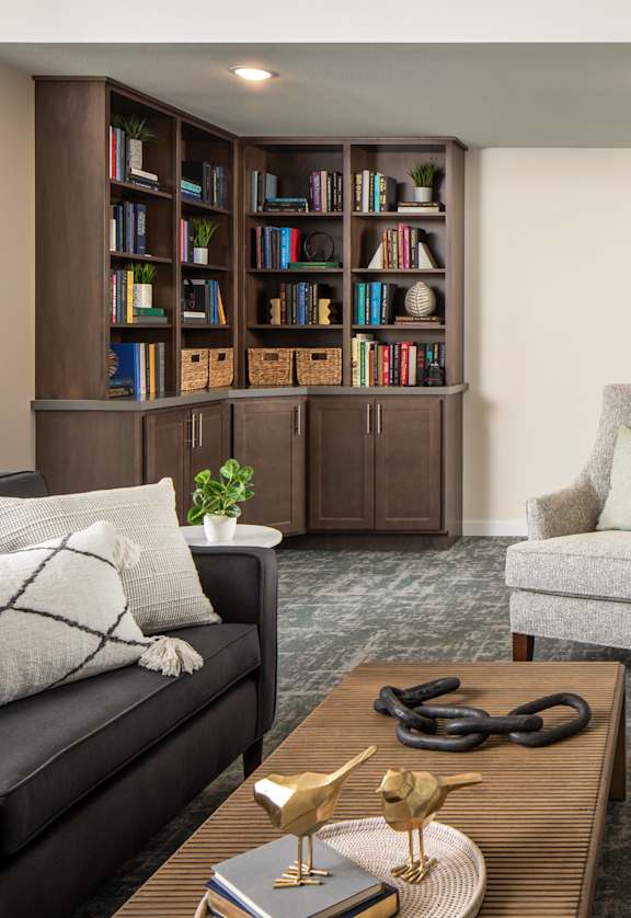 A living room with a black couch, a chair, a coffee table, and a bookshelf.