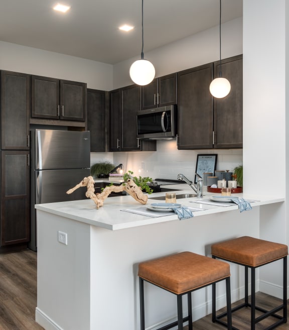 Modern kitchen with designer lighting, dark cabinetry, stainless steel appliances and counter with seating  at Chapter at the Streets of St Charles, Saint Charles, 63303