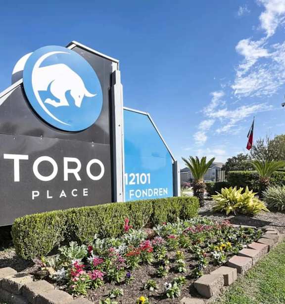A sign for Toro Place with a blue bear logo and a red pole with an American flag.