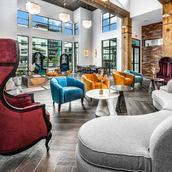 A red chair sits in a room with a grey couch and a wooden table.