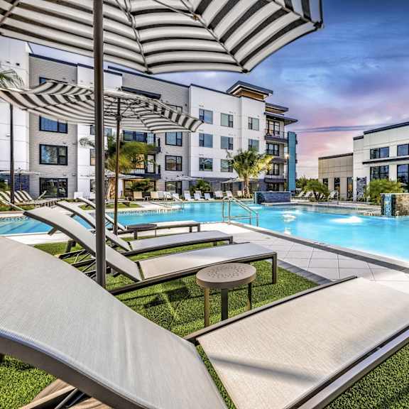 A pool area with sun loungers and umbrellas in front of a modern building.