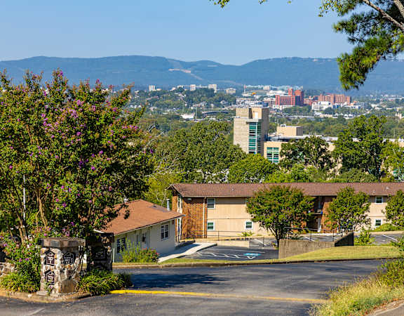 A building with a brown roof is surrounded by greenery and a parking lot.