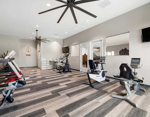 A gym with treadmills, exercise bikes, and a ceiling fan.