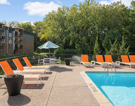 A pool area with orange chairs and a white umbrella.