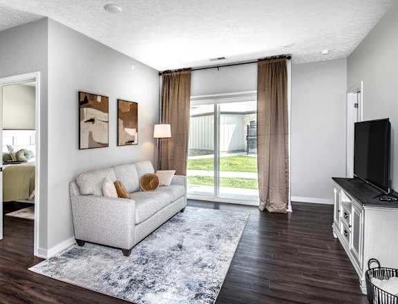 A living room with a grey couch, a television, and a large window with curtains.
