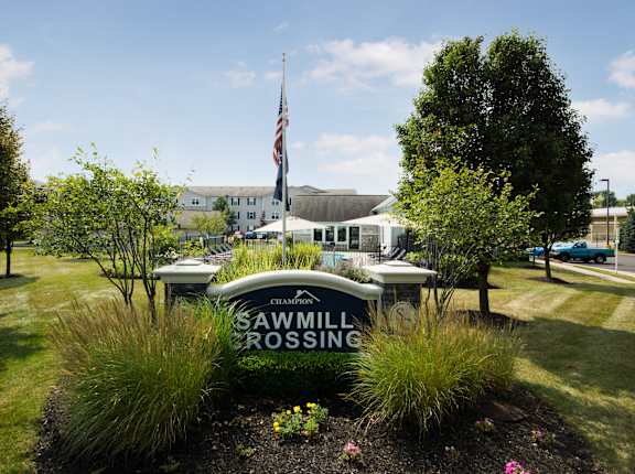 A sign that says Sawmill Crossing is in front of a grassy area.