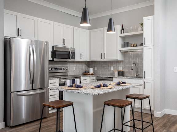A kitchen with a refrigerator, microwave, oven, and bar stools.at The Edison at Maple Grove, Maple Grove, 55311