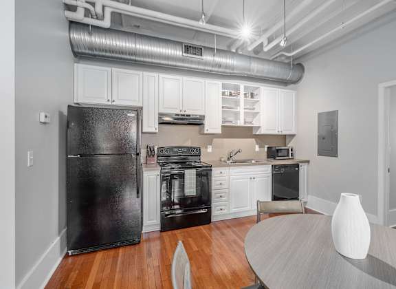 A black refrigerator is in a white kitchen with wooden floors.