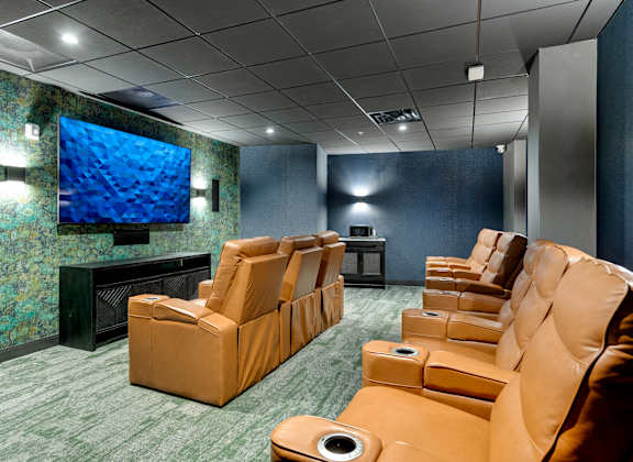 A row of brown recliner chairs are lined up in a room with a large screen television.