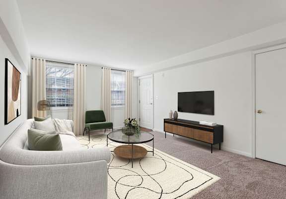 A living room with a grey couch, a green chair, a coffee table, and a television at The Fields of Bethesda, Chevy Chase, 20815