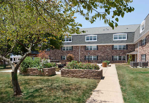 A building with a grey roof and a stone wall with a tree in front.