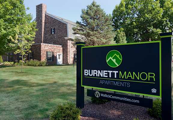 A sign for Burnett Manor Apartments stands in front of a brick building.