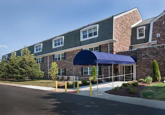 A building with a blue awning is surrounded by trees and bushes.