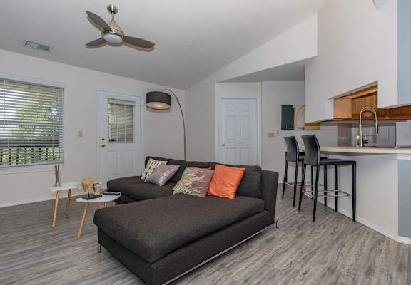A living room with a grey couch and a fan on the ceiling.