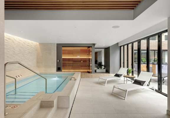 A modern indoor swimming pool with a wooden wall and lounge chairs.