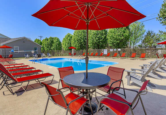 a pool with red chairs and a table with an umbrella at The Dylan, Murfreesboro, TN