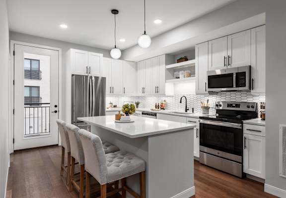 a kitchen with white cabinets and a large island with white chairs at The Flats & Terraces at Wildhorse Village, Chesterfield, MO