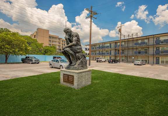 A statue of a man reading is in the middle of a grassy area. at The Cove at State Street Apartments, Baton Rouge, LA, 70802