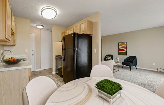 a living room with a dining room table and a kitchen with a refrigerator at Northtown Village Apartments, Spring Lake Park, 55432-2650