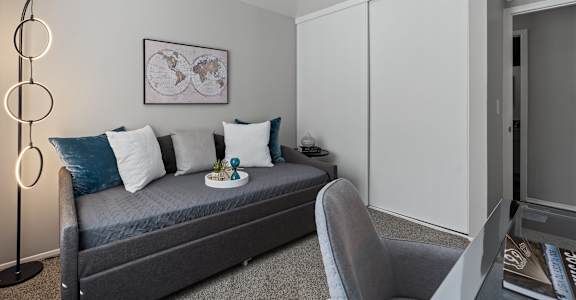 A modern bedroom with a grey bed, a grey chair, a white cabinet, and a framed world map on the wall.