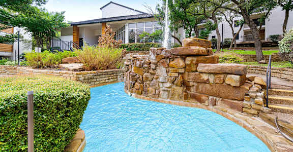 a swimming pool with a waterfall and a house in the background