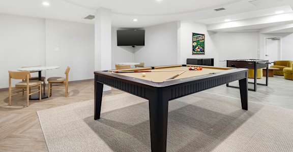 A billiard table is in the middle of a room with a TV mounted on the wall.