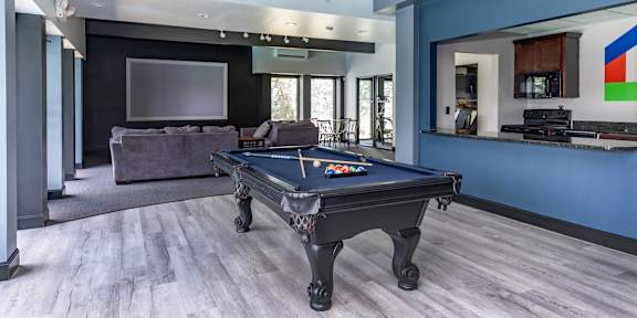 A shiny air hockey table is in the middle of a room with chairs and a kitchen in the background.