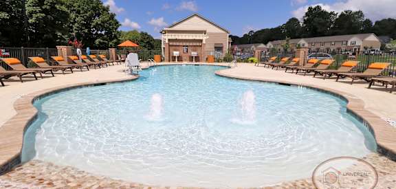 A large swimming pool with a fountain in the middle surrounded by sun loungers.