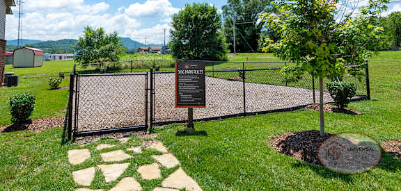 a park with a sign in front of a fence and a tree