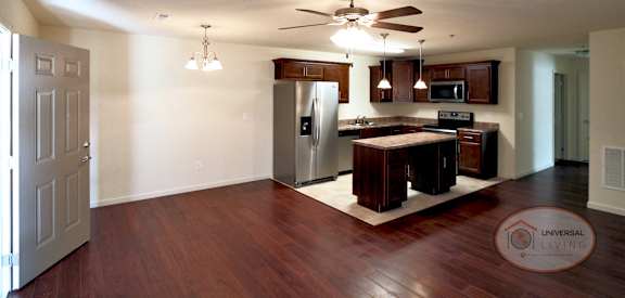 an empty living room with a kitchen and a ceiling fan