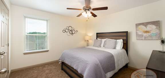 A bedroom with a bed, a ceiling fan, and a painting on the wall.