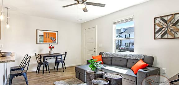 A living room with a grey couch, a dining table with chairs, and a ceiling fan.