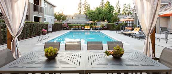 a pergola with a wooden table and chairs in front of a swimming pool