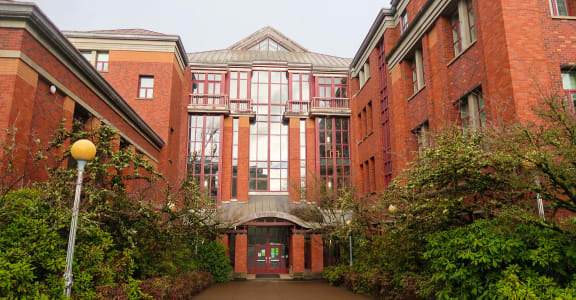a walkway between two large red brick buildings with trees on both sides of the walkway