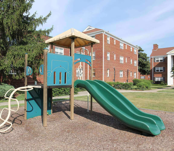 a playground with a green slide and a red brick building in the background at Parkland Village, Forestville, MD 20747