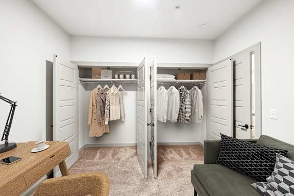 A room with a desk, chair, and a closet with clothes